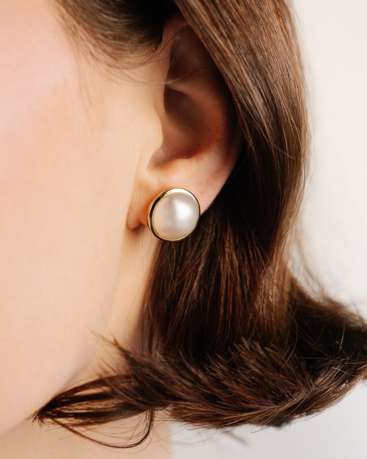 Mabe Pearl earring featuring our Australian South Sea Mabe pearl set in hypoallergenic gold worn by a person with a neutral background