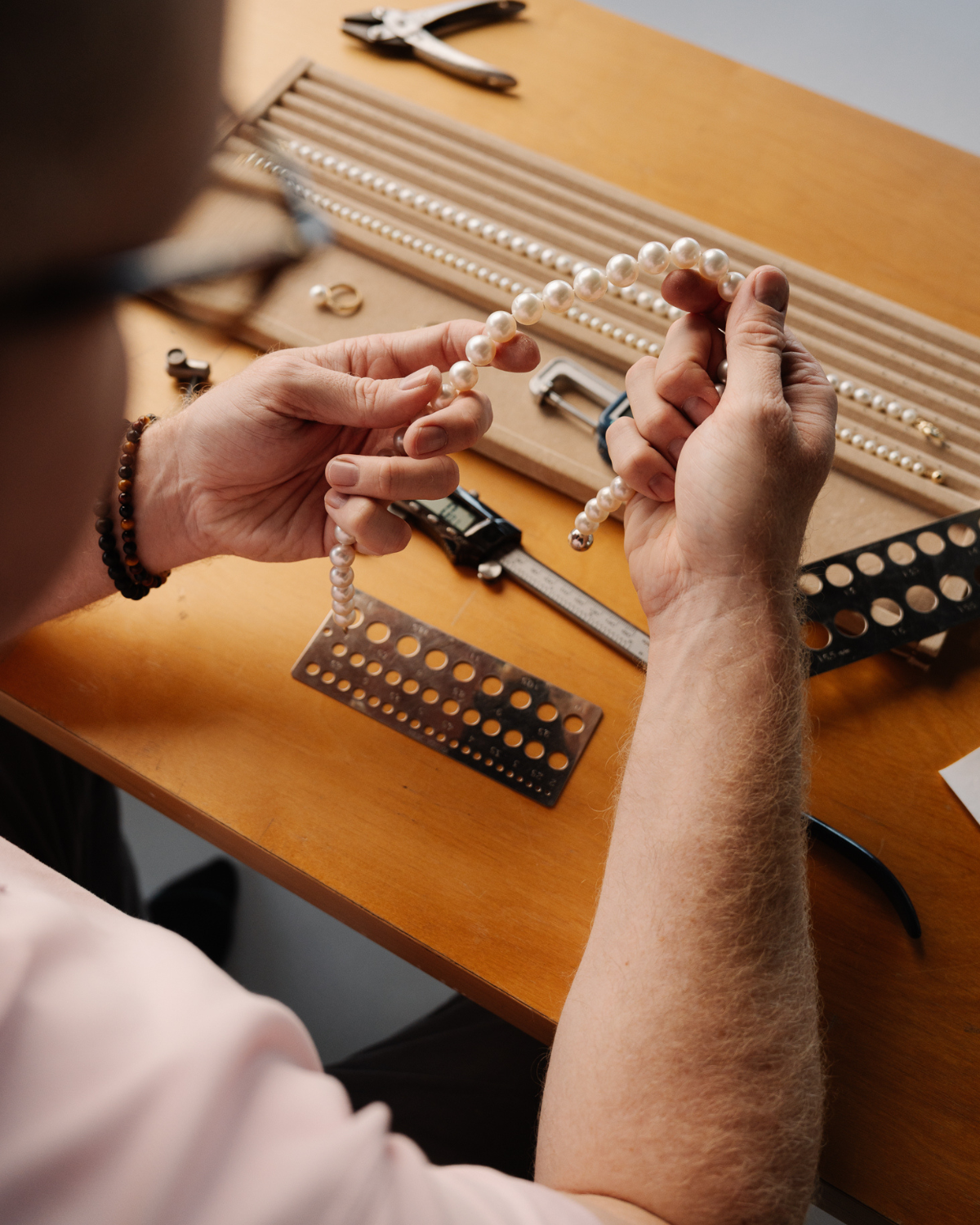 Our jewellery working with our Australian South Sea pearls and jewelry-making tools on a wooden table to create hypoallergenic jewellery pieces.