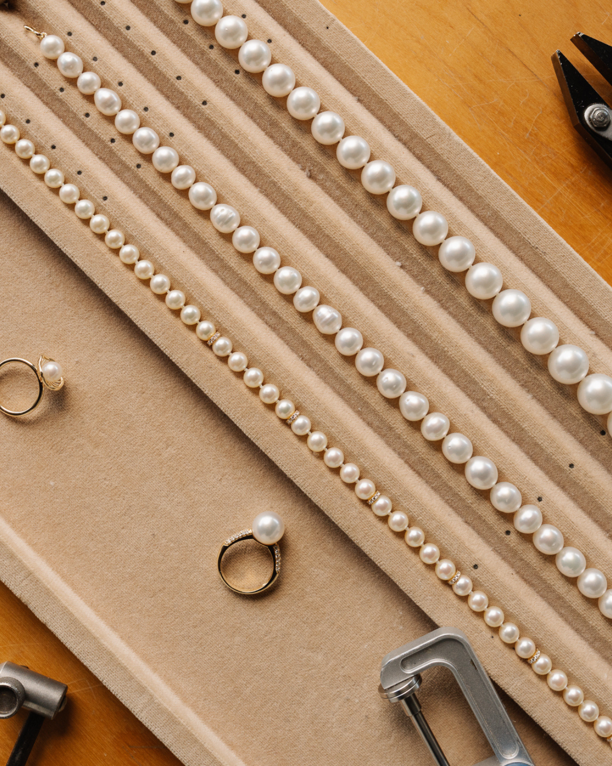 Pearl strand necklaces and pearl ruings on a display stand with jewelry tools on a wooden surface, all easy to wear and hypoallergenic jewellery options. 