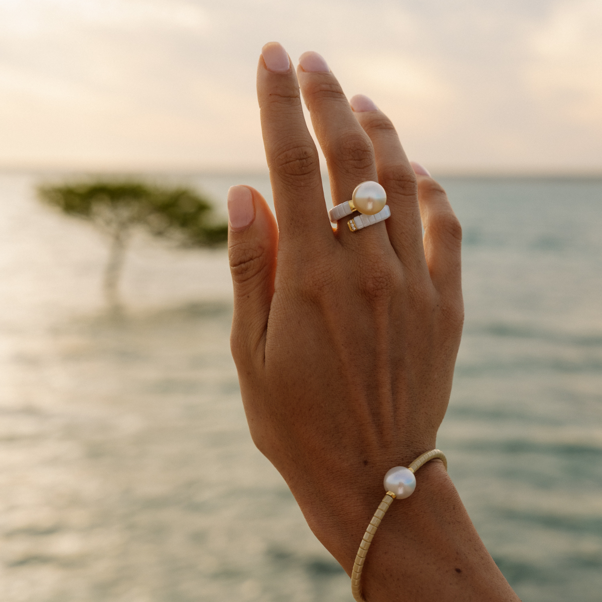 A person holds their hand up, wearing an expandable ceramic pearl ring featuring a gold Australian South Sea pearl and a matching bracelet.