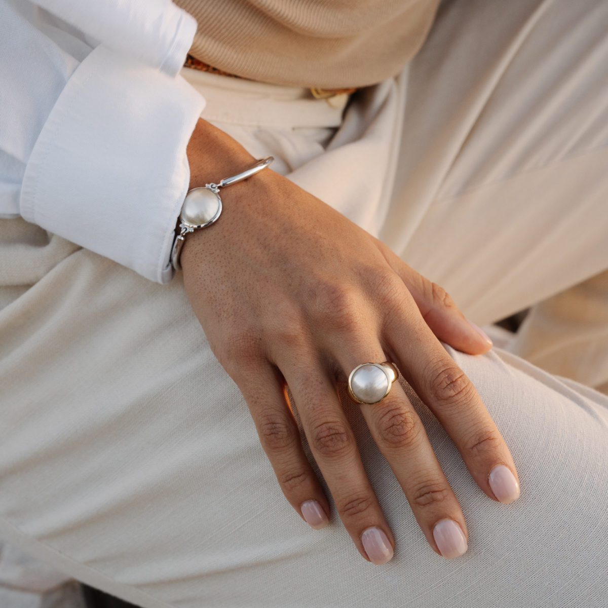 Hand wearing a mabe pearl ring and bracelet jewelery set on a neutral background