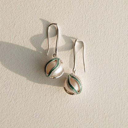 Pair of silver pearl earrings with green accents on a beige background
