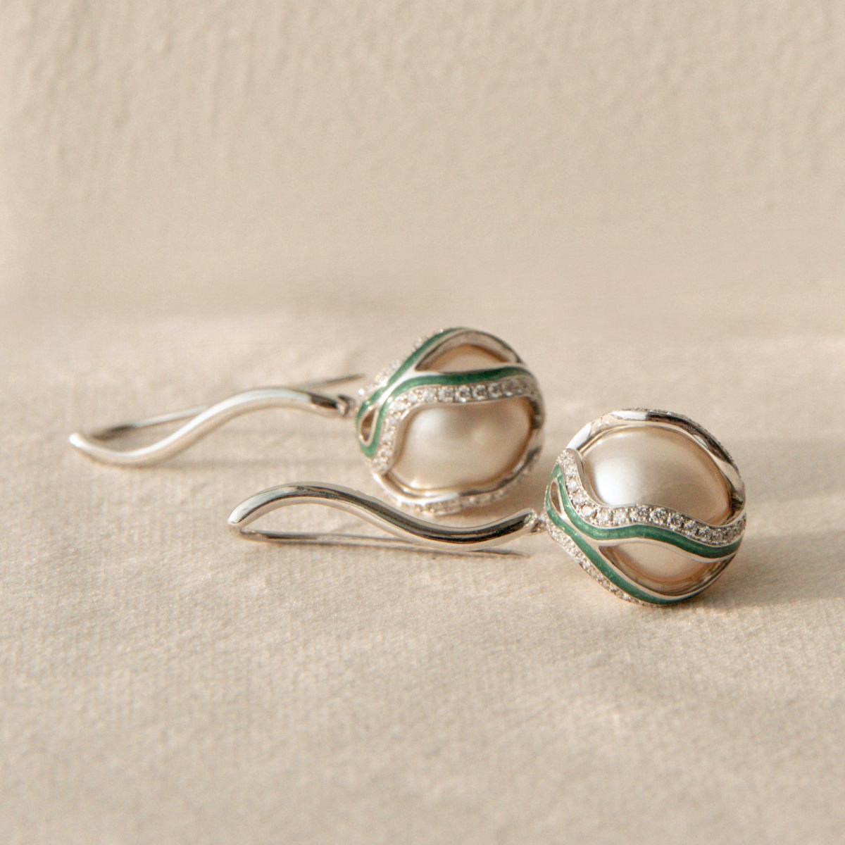 Pair of silver pearl earrings with green accents on a beige surface