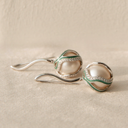 Pair of silver pearl earrings with green accents on a beige surface