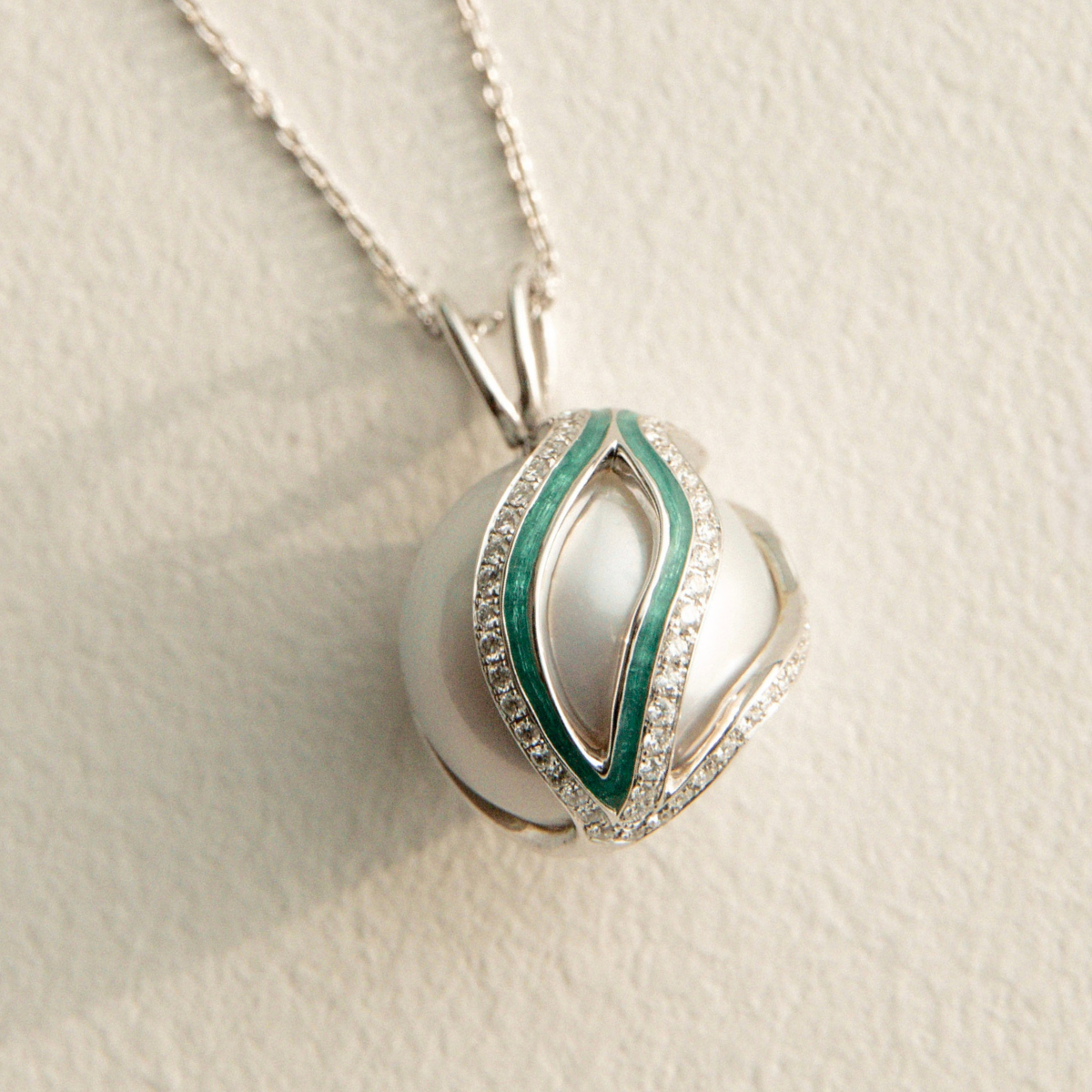 Silver pearl pendant with green accents on a light beige background