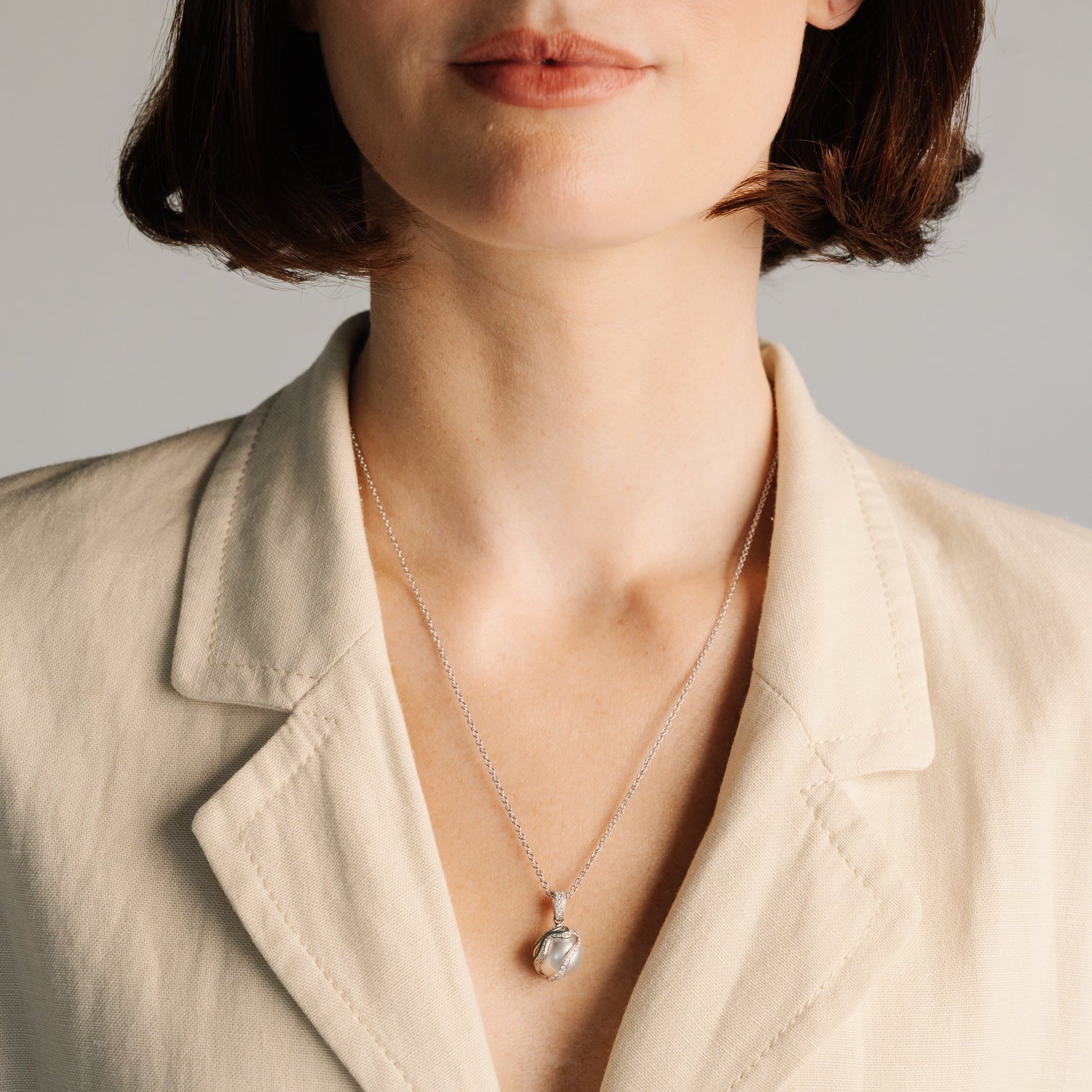 Person wearing a necklace with a pendant against a neutral background