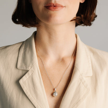 Person wearing a necklace with a pendant against a neutral background