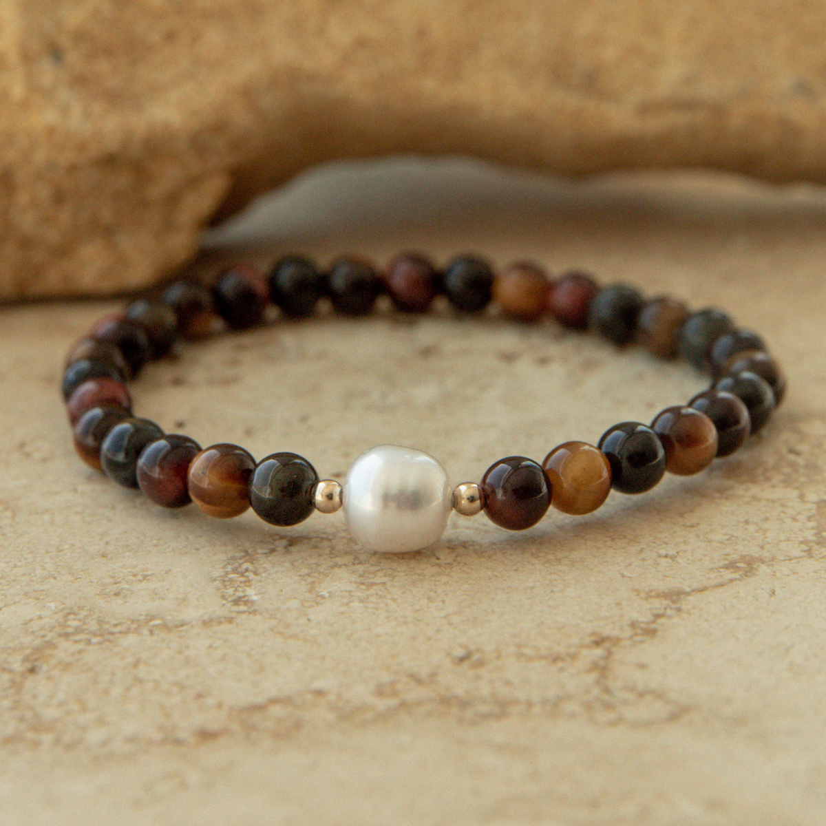 Beaded tiger eye bracelet with a pearl on a textured stone surface