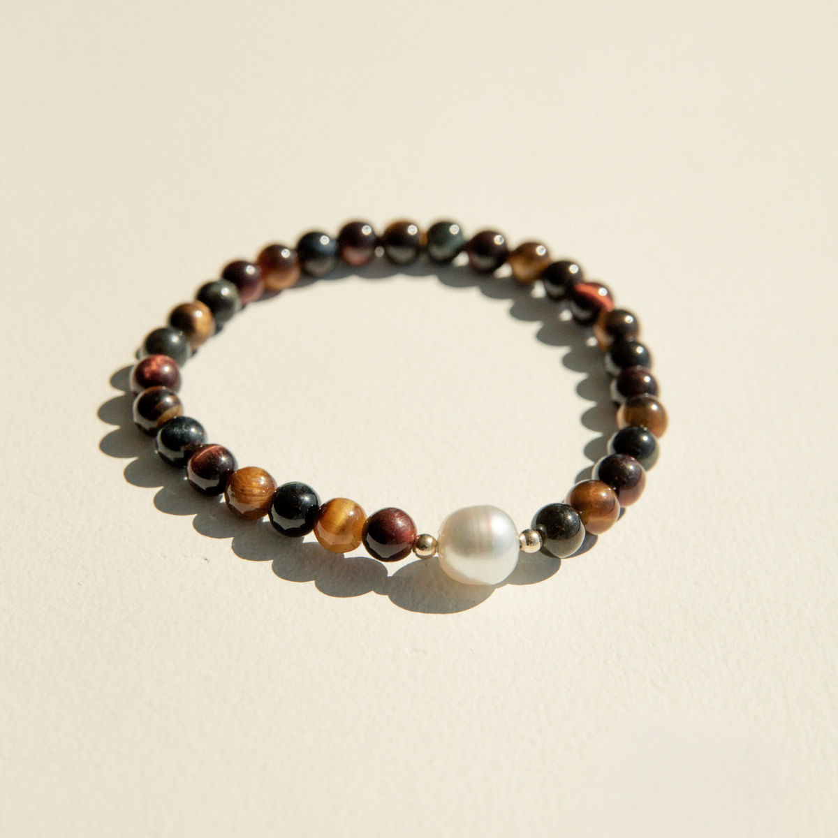 Bracelet with multicolored tiger eye beads and a pearl on a beige background