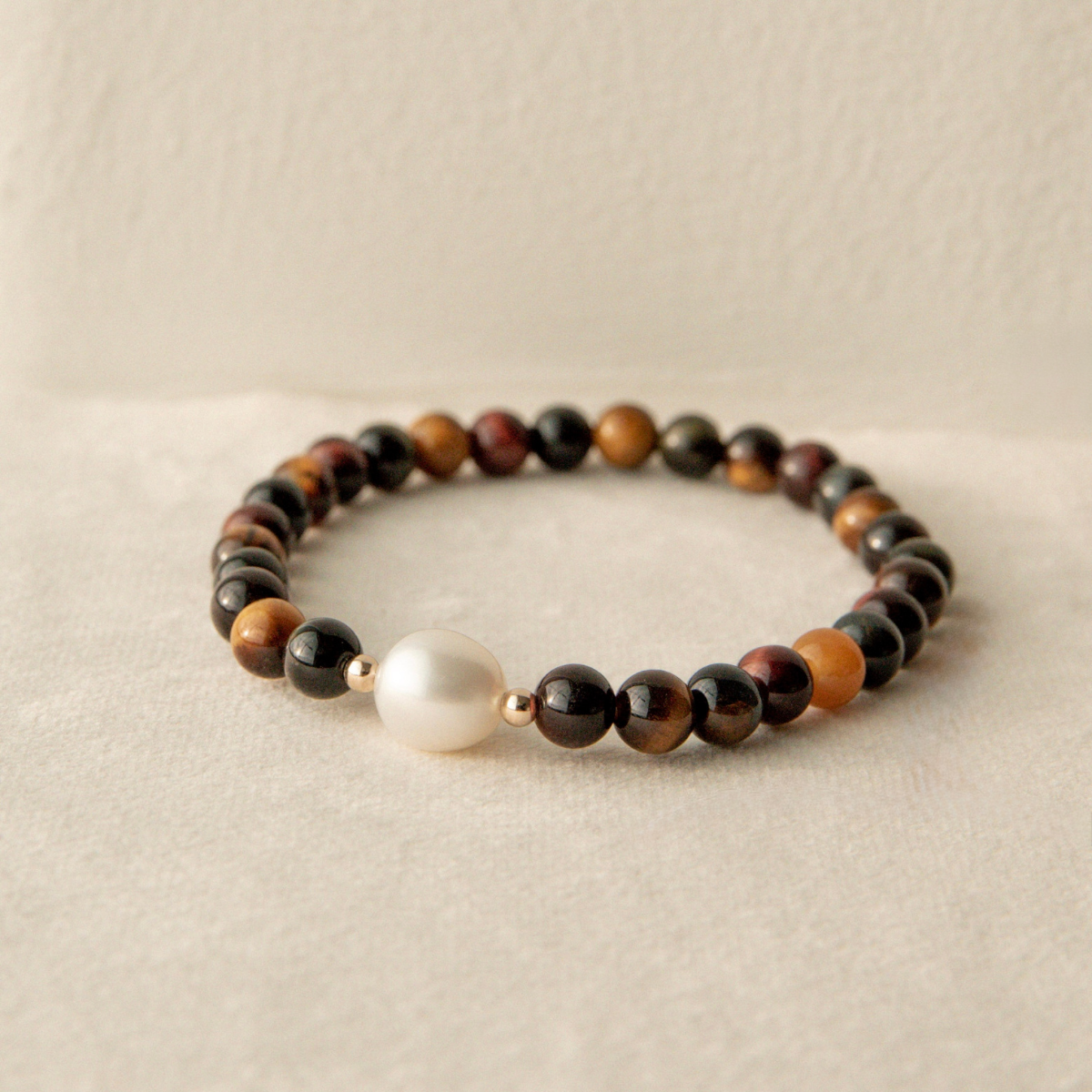 Tiger eye beaded bracelet with a pearl on a beige background