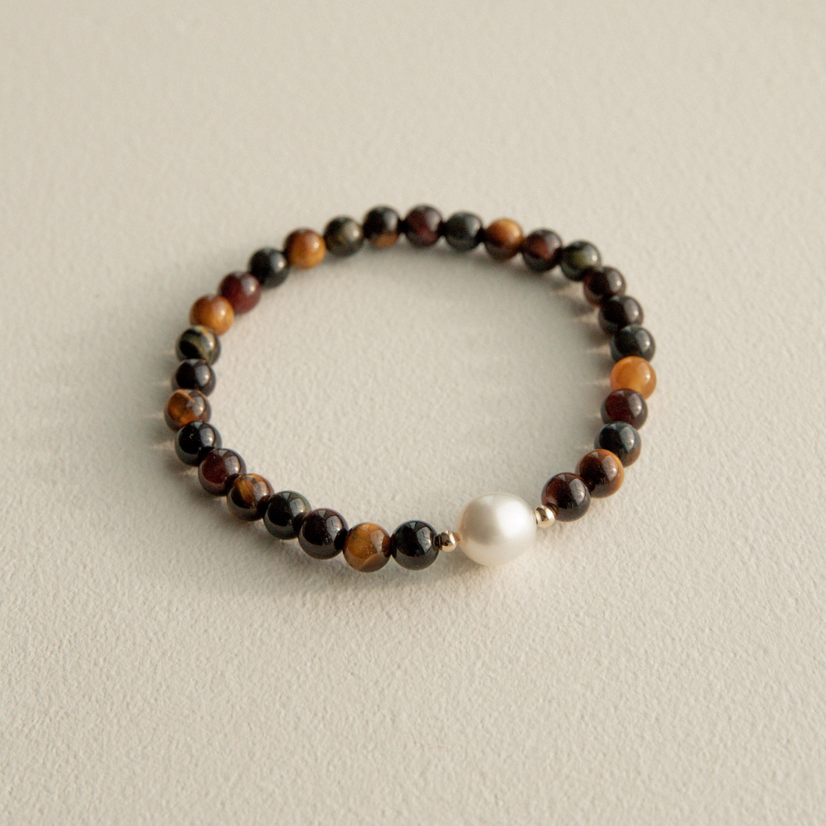 Bracelet with multicolored tuger eye beads and a pearl on a light beige background