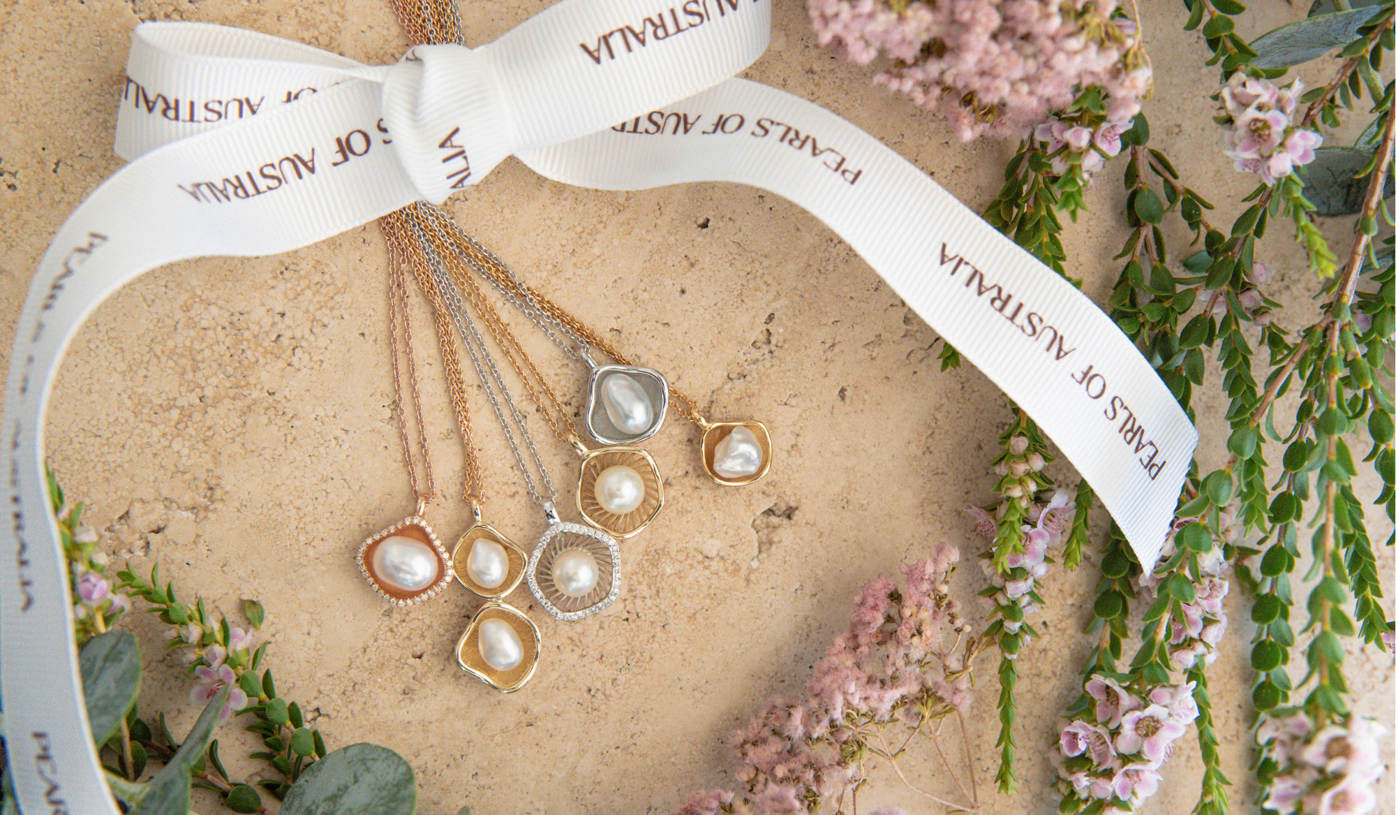 Gold pearl necklaces on a beige surface with a white ribbon and floral decorations.