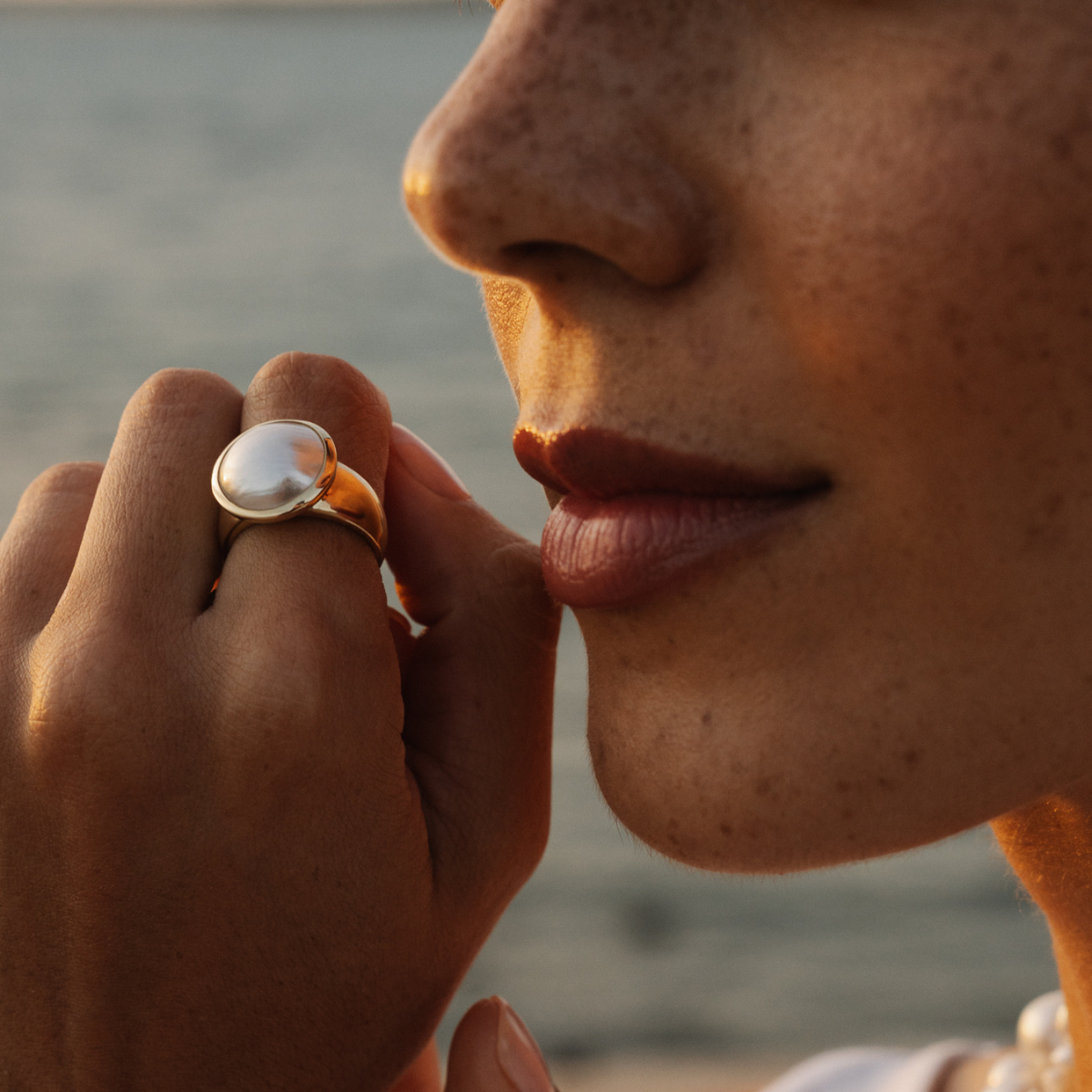 Close-up of a person wearing a large mabe pearl ring on their finger, with a blurred background.