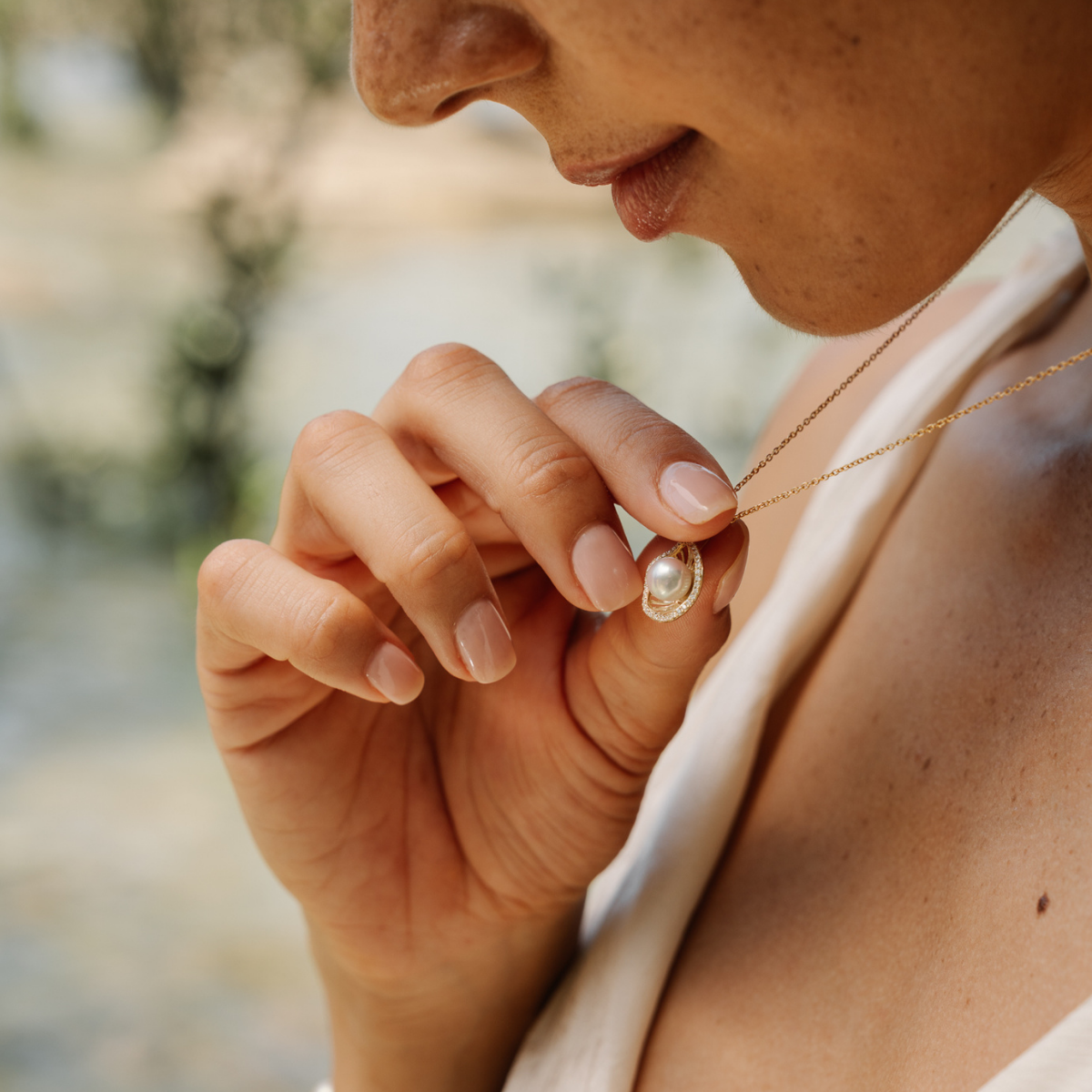 Close-up of a person wearing a pearl necklace set in yellow gold with a blurred natural background