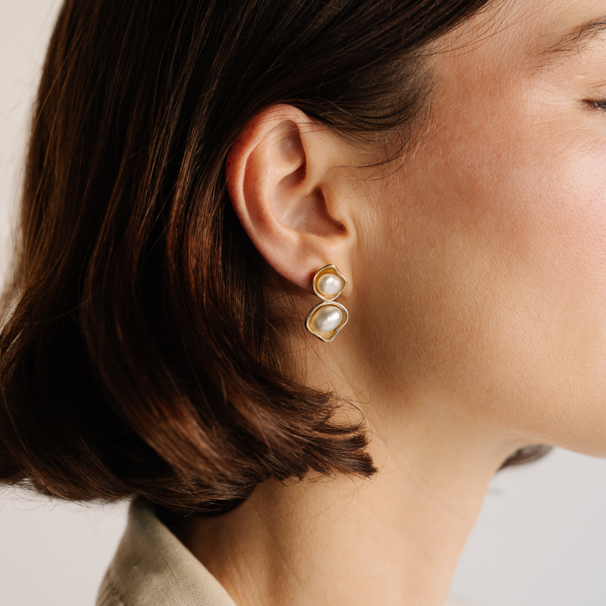 Close-up of a person wearing yellow gold earrings featuring our Australian South Sea Keshi pearls grown at our Cygnet Bay pearl Farm with a neutral background