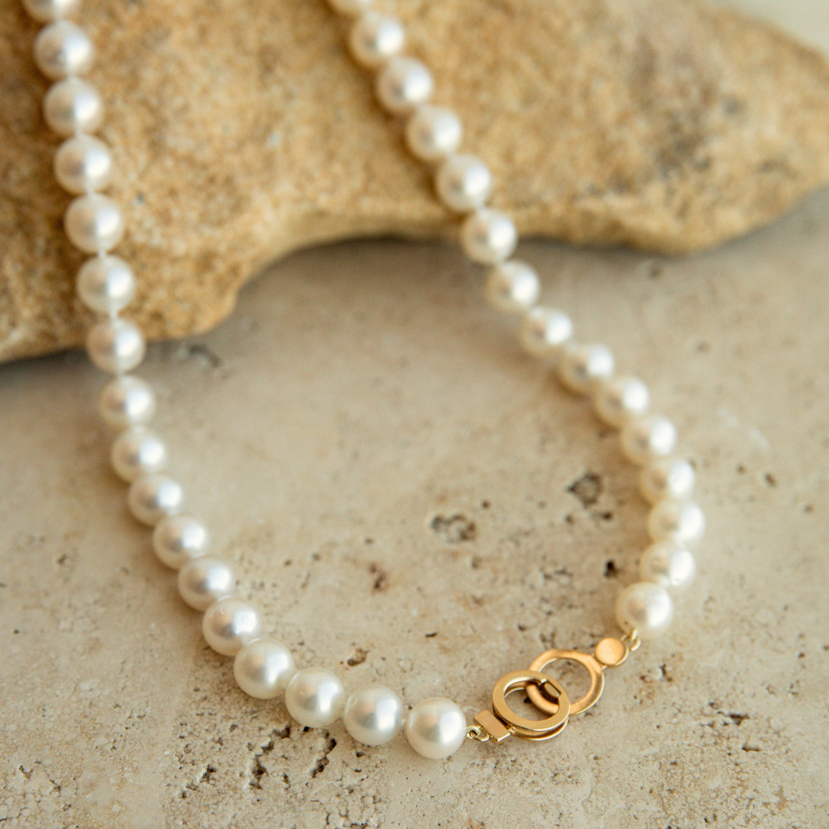 Pearl strand necklace with a gold circle clasp on a textured stone surface