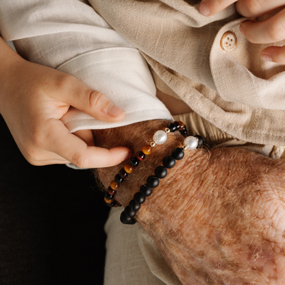 Close-up of a child's hand holding two pearl bracelets with beads on a Dad's hand.