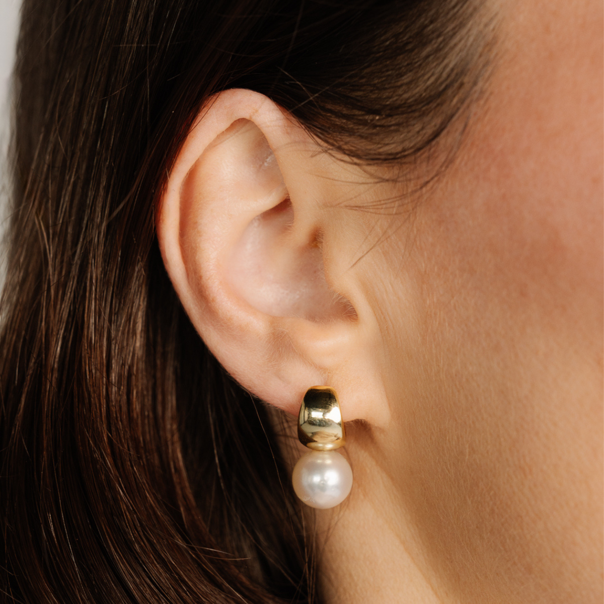 Gold earring with a pearl on an ear