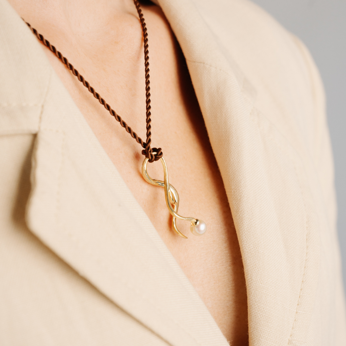 Gold necklace with a pearl pendant on a person wearing a beige coat.
