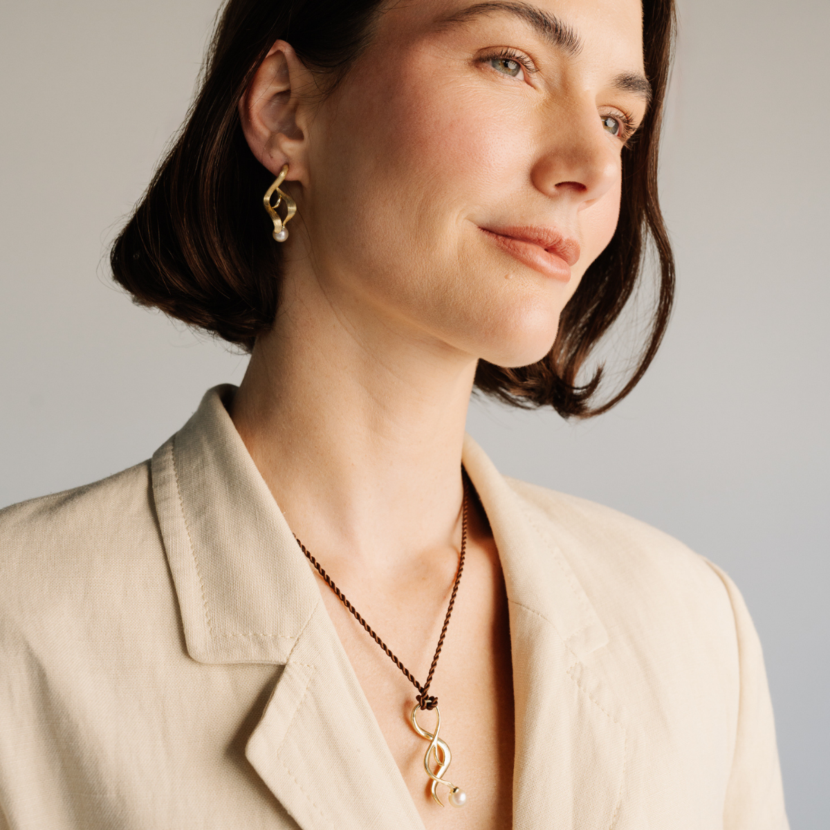 Woman wearing a silk cord necklace with a unique pearl pendant and matching earrings against a neutral background