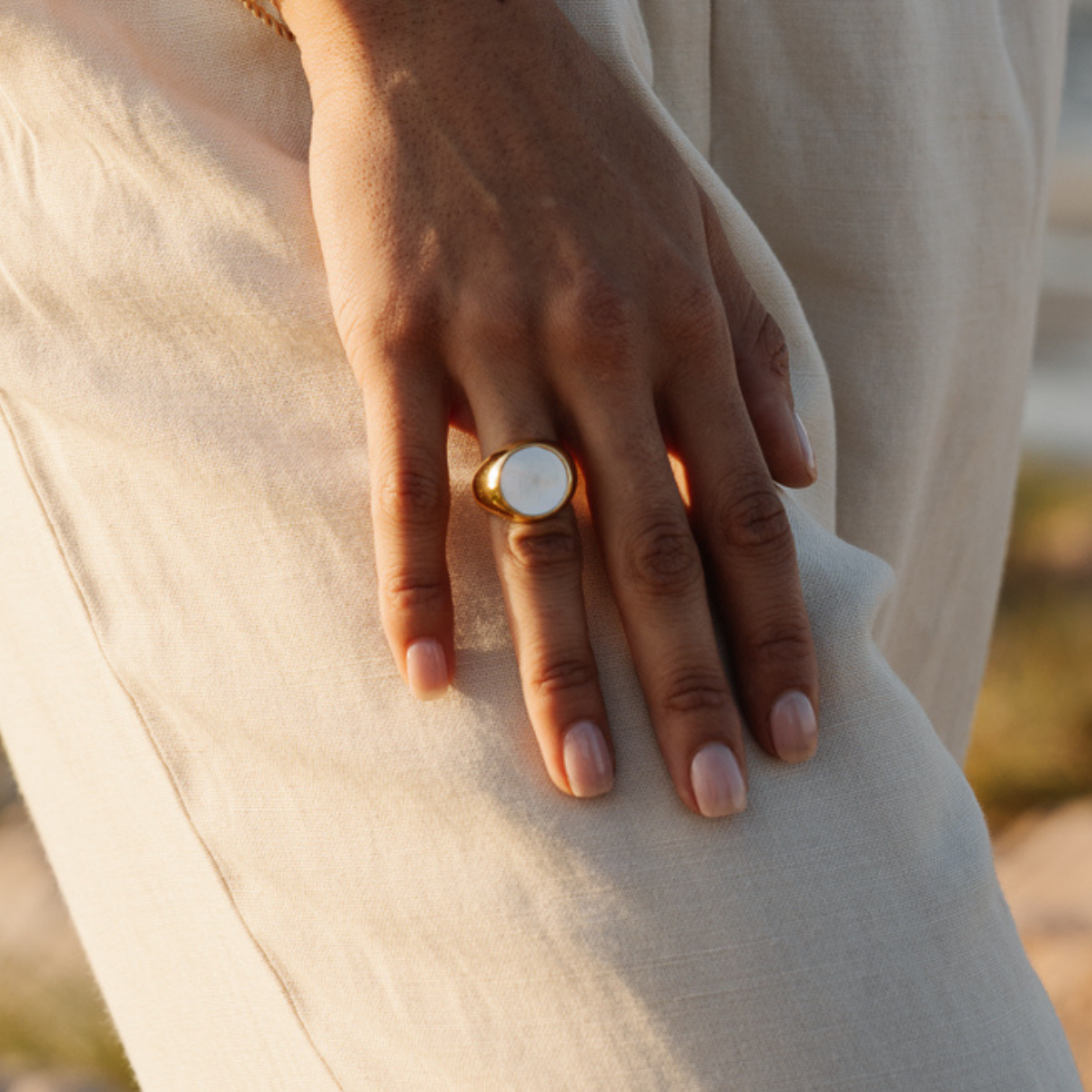 Hand wearing a gold mother of pearl signet ring holding a beige fabric