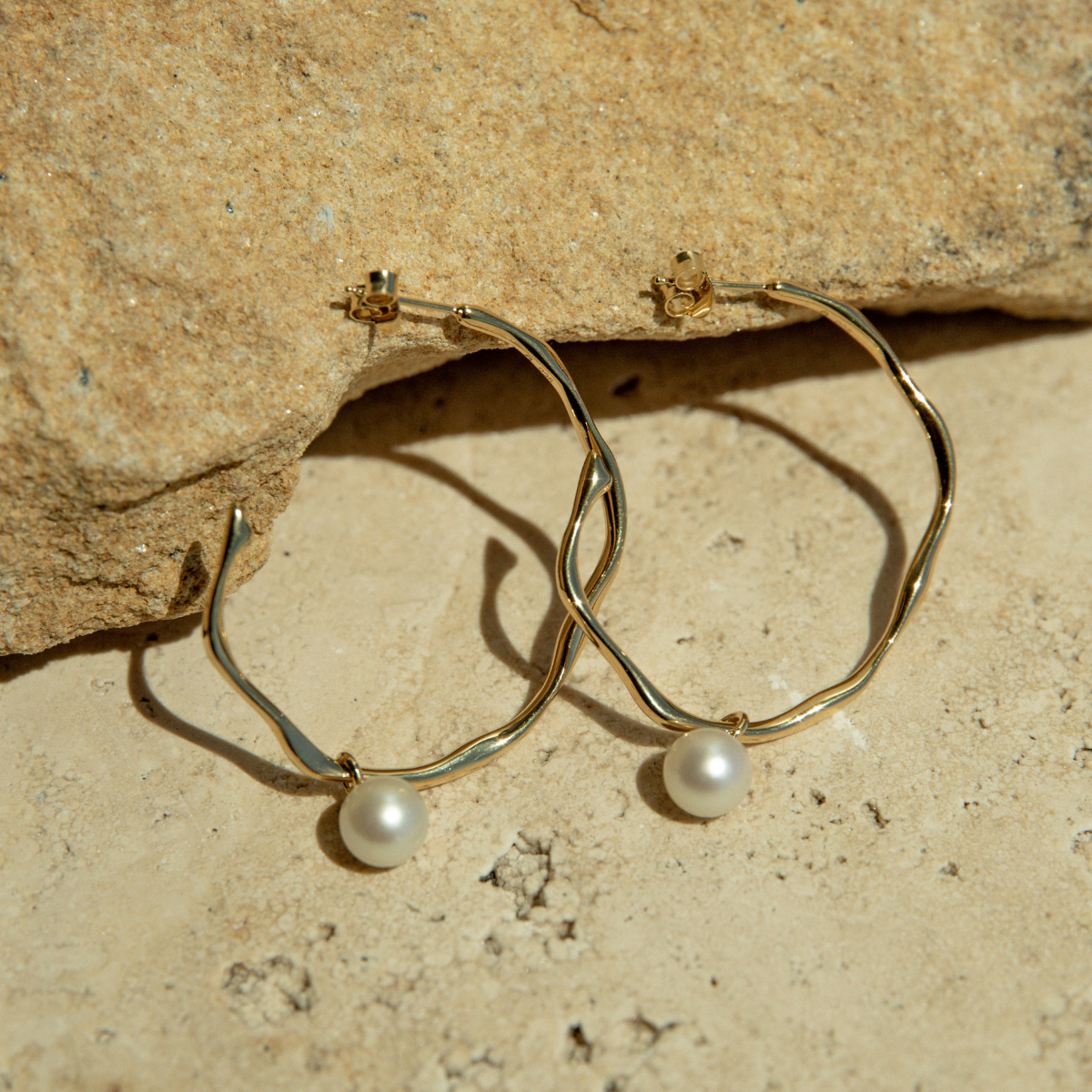 Gold hoop earrings with pearls on a stone surface