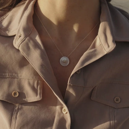 A woman wears her stunning Mother of Pearl button necklace that has a button motif on a delicate chain. 