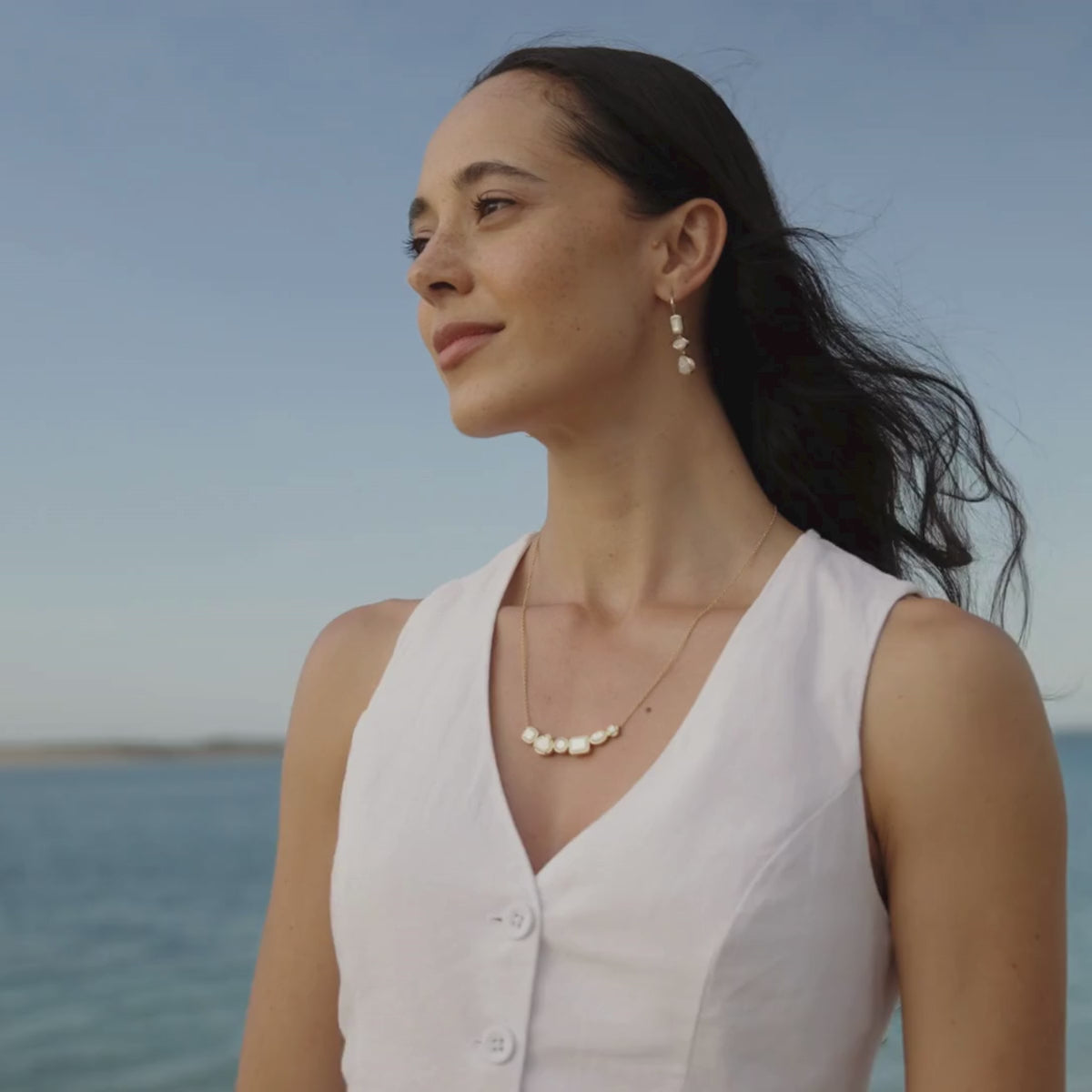 A woman wears her beautiful Radiance Mother of Pearl Medley Necklace and matching earrings that feature our Cygnet Bay grown Australian Mother of Pearl Shell that has been faceted to resemble traditional diamond cuts like emerald cut, pear cut, princess cut, and oval cut set in a bezel setting.