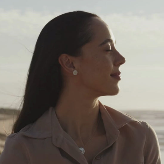 A woman wears her Mother of Pearl Button Studs and matching Mother of Pearl Button Chain Necklace as she looks over the horizon, basking in the rising sun at our Cygnet Bay Pearl Farm.