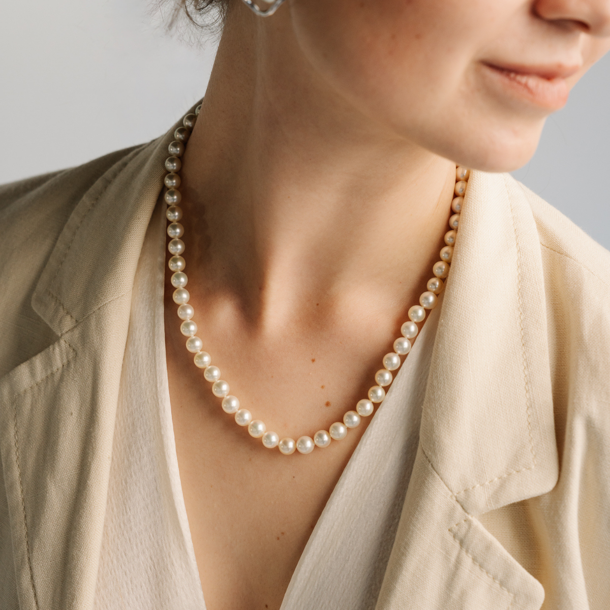 Person wearing a pearl necklace with a neutral background