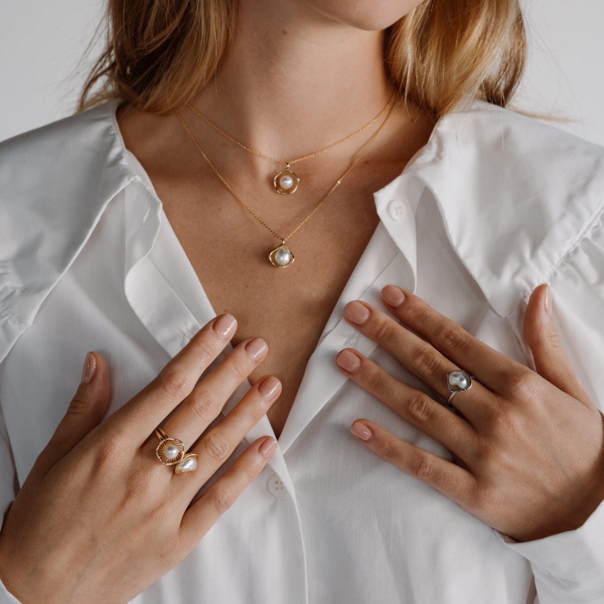 Close-up of a person wearing gold necklaces and rings with a white shirt.